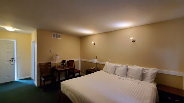 A hotel room with a bed, a desk, a chair, a nightstand, and a lamp.