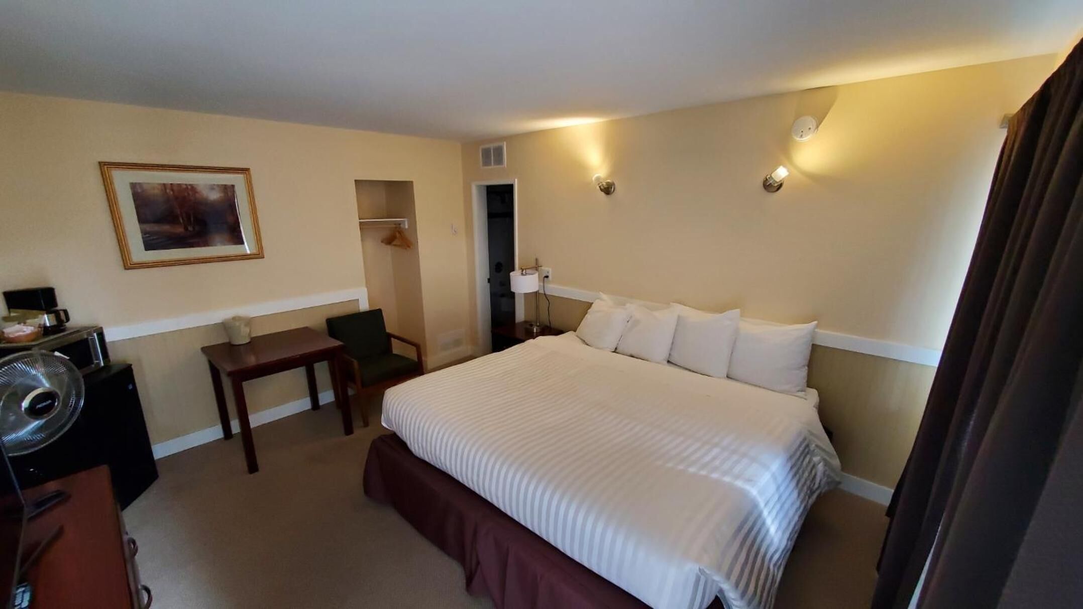 Hotelkamer met een groot bed, een bureau, een stoel, een klein tafeltje en een lijst aan de muur.