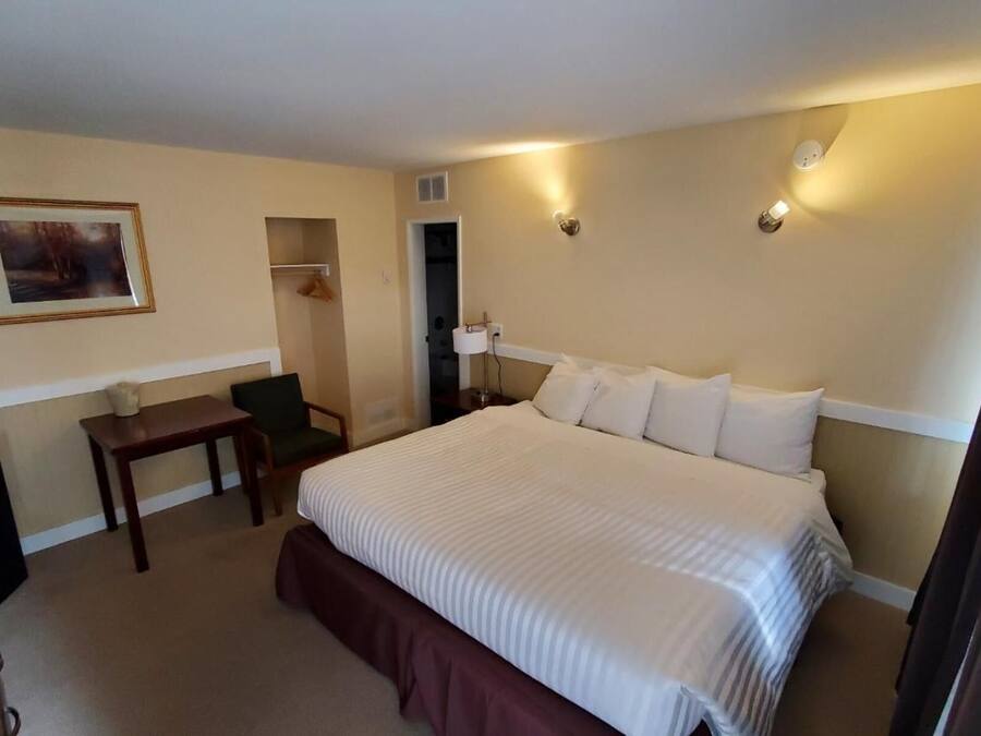 A hotel room with a large bed, a desk, a chair, a small table, and a framed picture on the wall.