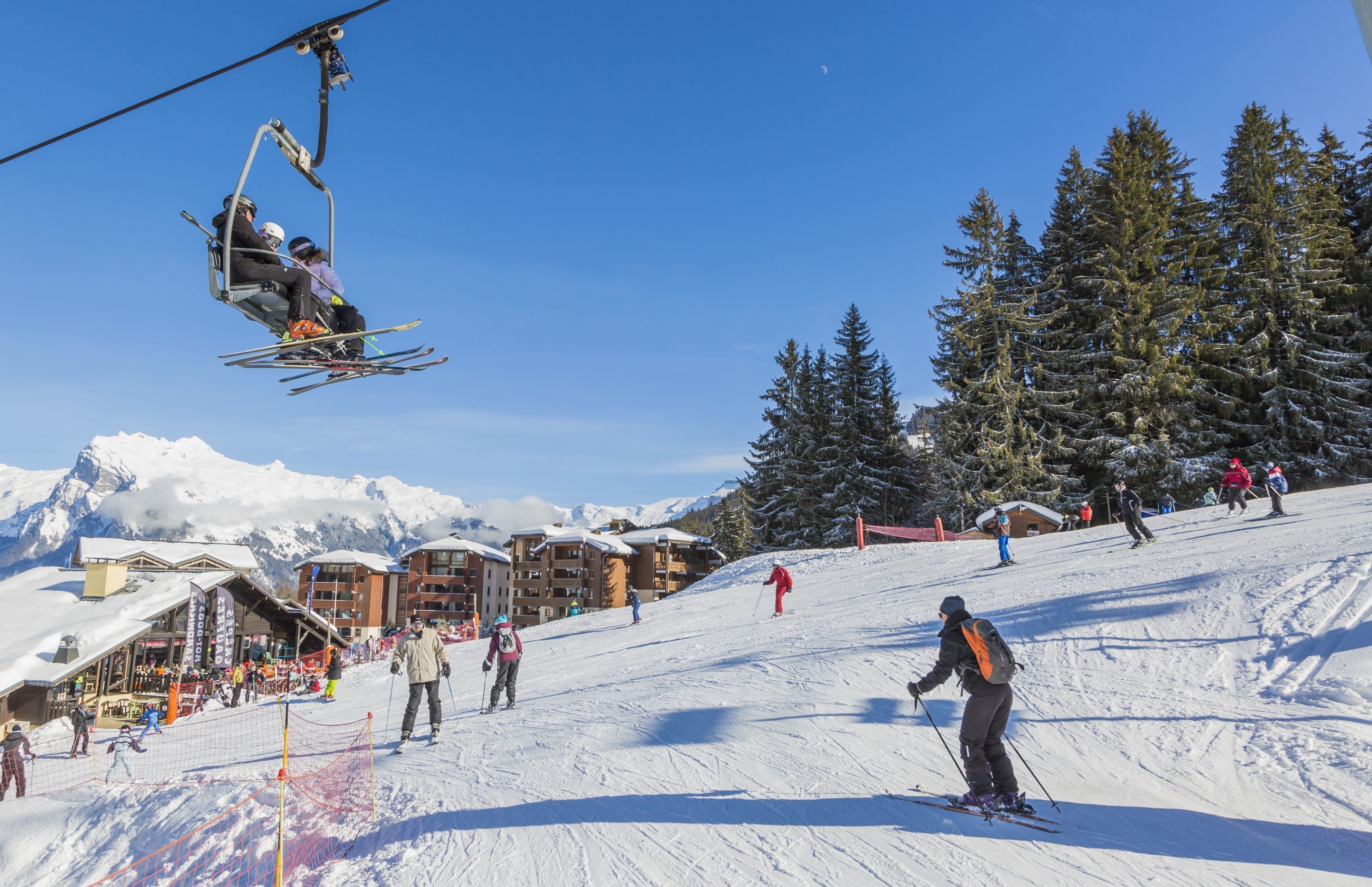 Une station de ski dotée d’un télésiège, de pistes enneigées et de bâtiments visibles au loin.