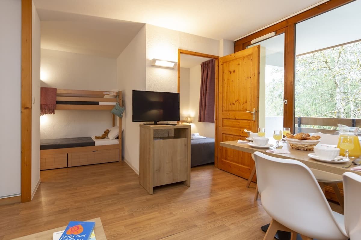 A cozy room with a bunk bed, a TV, a dining table with breakfast items, and a large window.