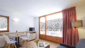 En moderne stue med spiseplads, en sofa, et sofabord med bøger og et fjernsyn.