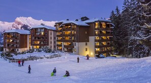 Un hotel a più piani con balconi, immerso in un paesaggio innevato e affacciato su montagne.
