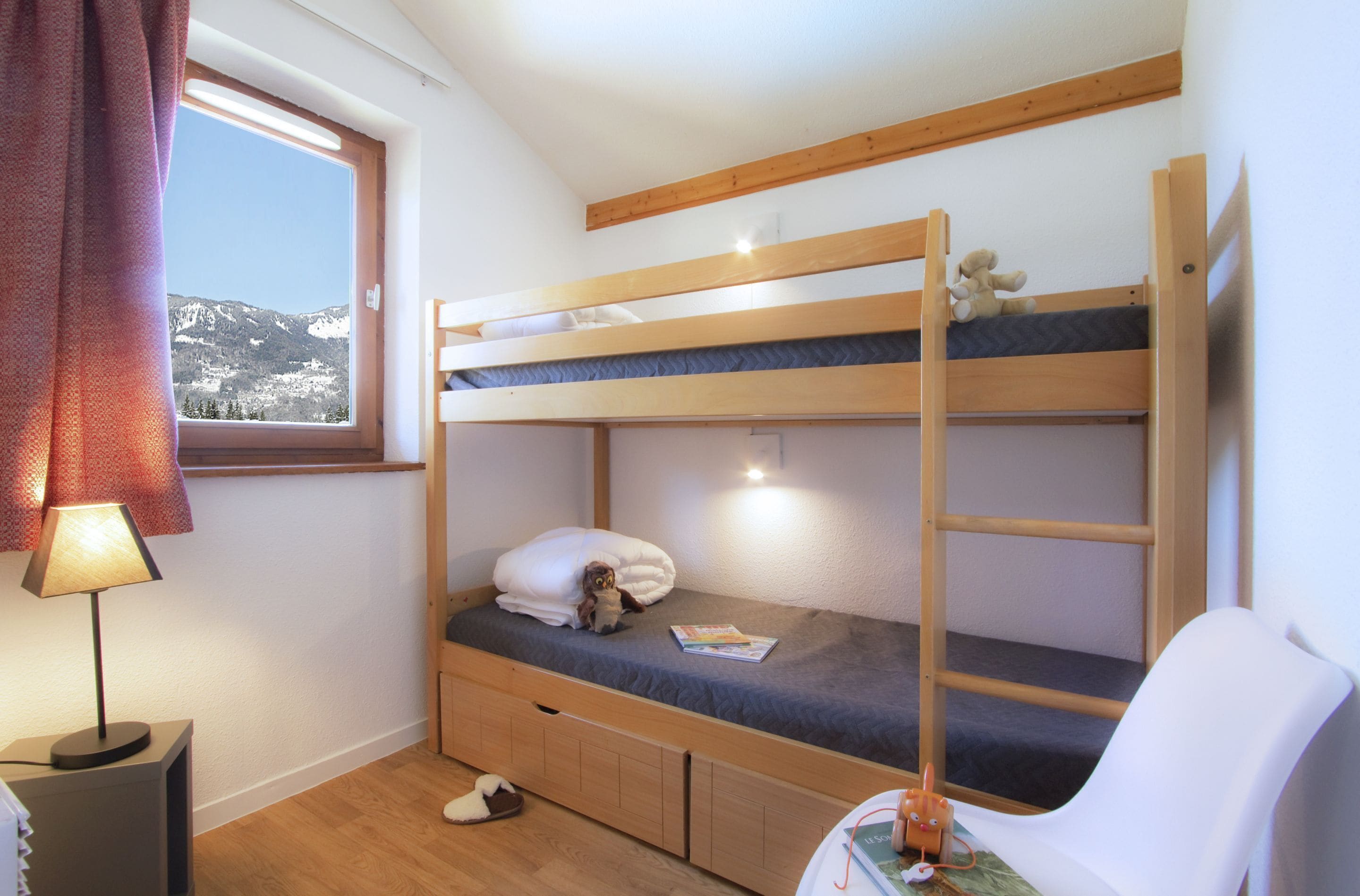 A bunk bed room with a window, a lamp, and a chair.