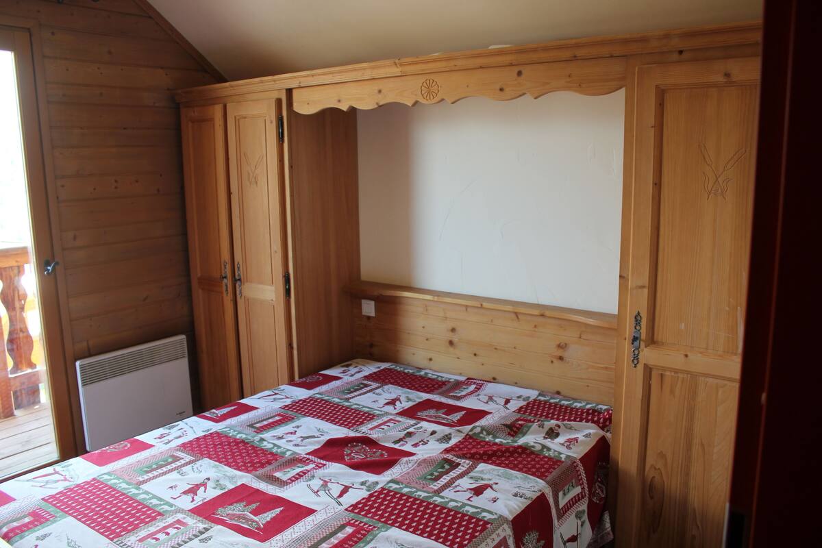 A wooden room with a bed, a radiator, and a door.