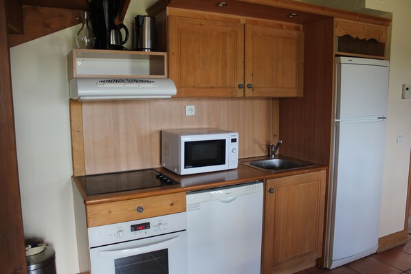 A compact kitchen with wooden cabinets, a microwave, a dishwasher, and a refrigerator.