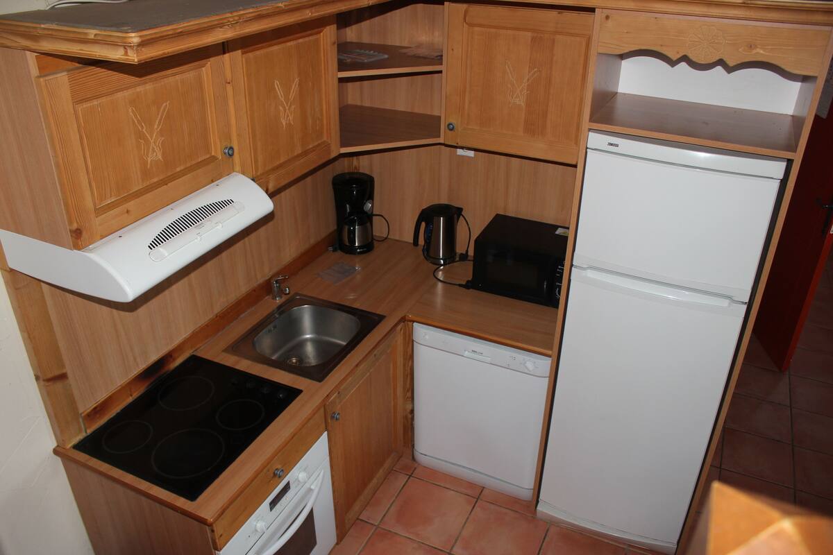 A compact kitchen with wooden cabinets, a built-in stove, a sink, a dishwasher, and a refrigerator.