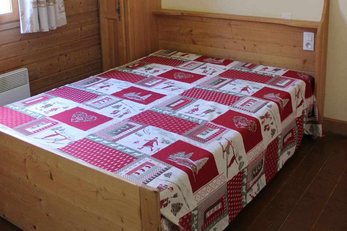 A wooden bed with a quilt in a room with wooden walls and a sloped ceiling.
