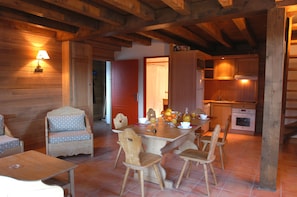 Ein rustikales Holzinterieur mit Essbereich, Holzstühlen, einem Tisch mit einer Vase Orangen und einer Küche mit Holzausbau.