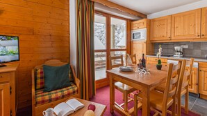 Ein gemütliches Zimmer mit einer hölzernen Sitzbank, einem Esstisch mit Stühlen, einem Fernseher und einer Küchenzeile mit Holzschränken und einer Mikrowelle.