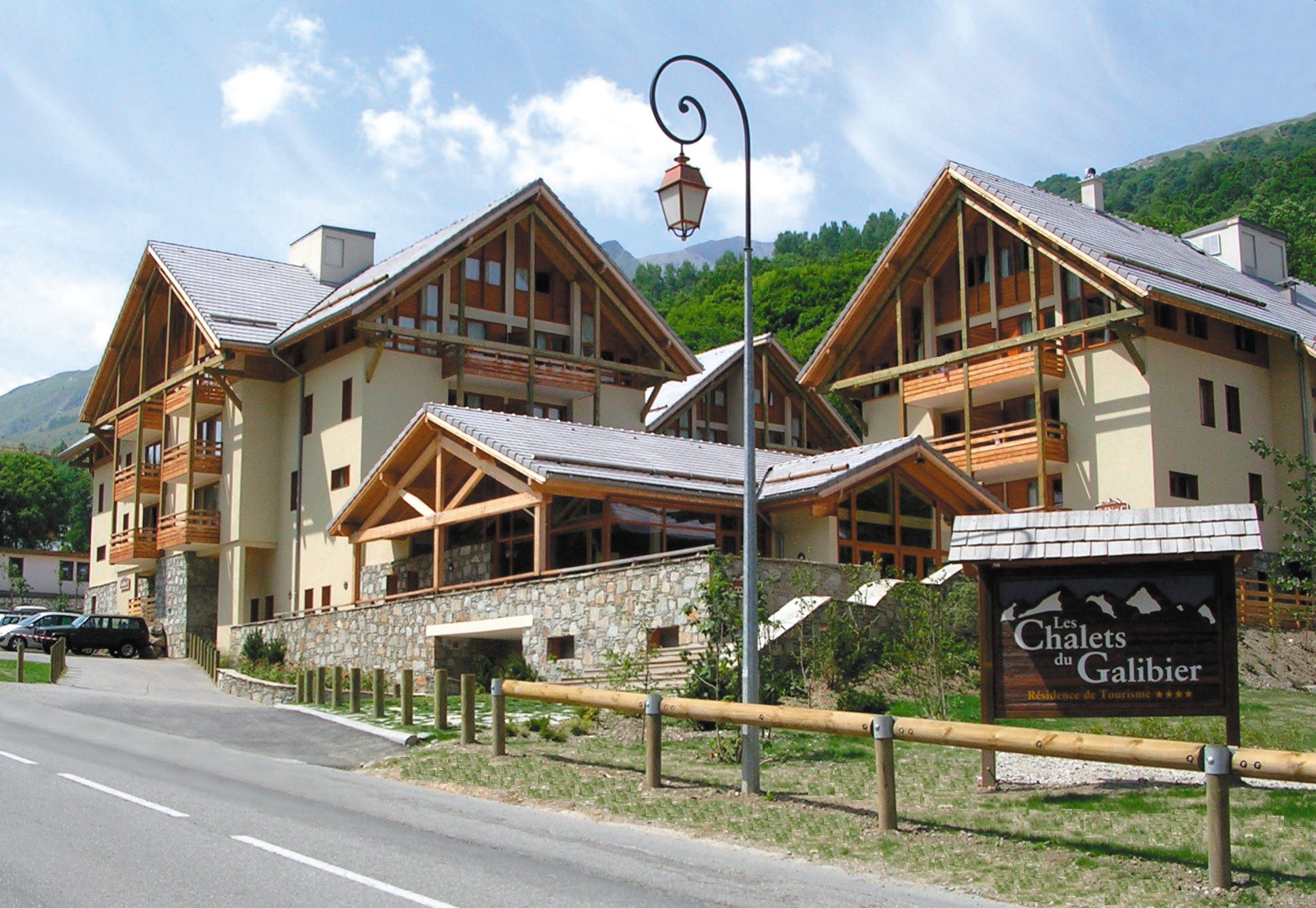 Un bâtiment de style chalet, doté de nombreux balcons, de fondations en pierre et d’une enseigne indiquant qu’il s’agit d’une résidence touristique.