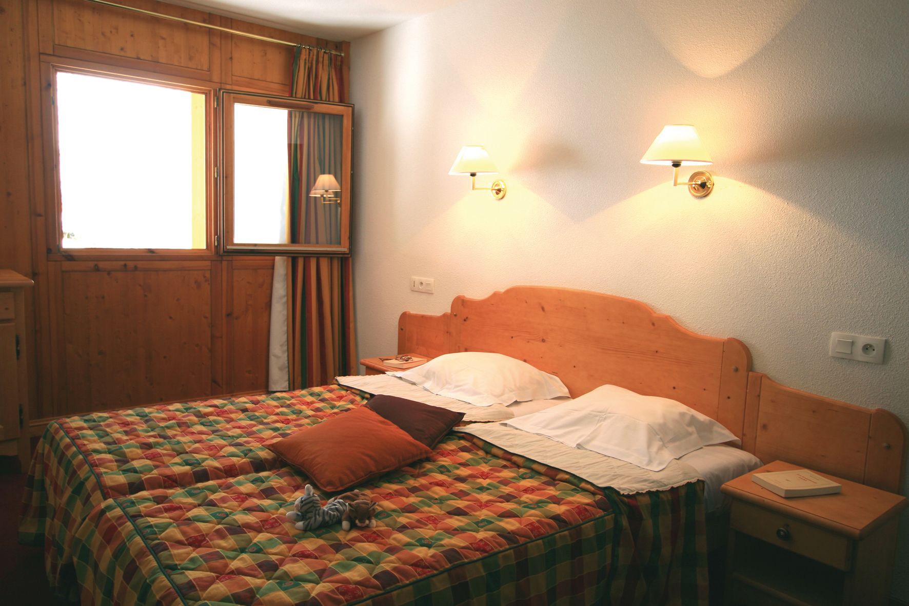 Une chambre à coucher avec une tête de lit en bois, deux lampes de chevet, une couvre-lit matelassé et une fenêtre avec des rideaux.