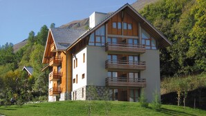 Ein großes, mehrstöckiges Gebäude mit Holzfassade und mehreren Balkonen, umgeben von üppiger Vegetation und Bergen.