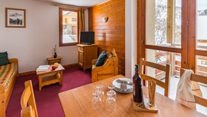 Ein gemütliches Zimmer mit Holzvertäfelung, einem Bett, einem kleinen Tisch mit Weingläsern, einem Fernseher und einem Fenster mit Blick auf eine verschneite Landschaft.