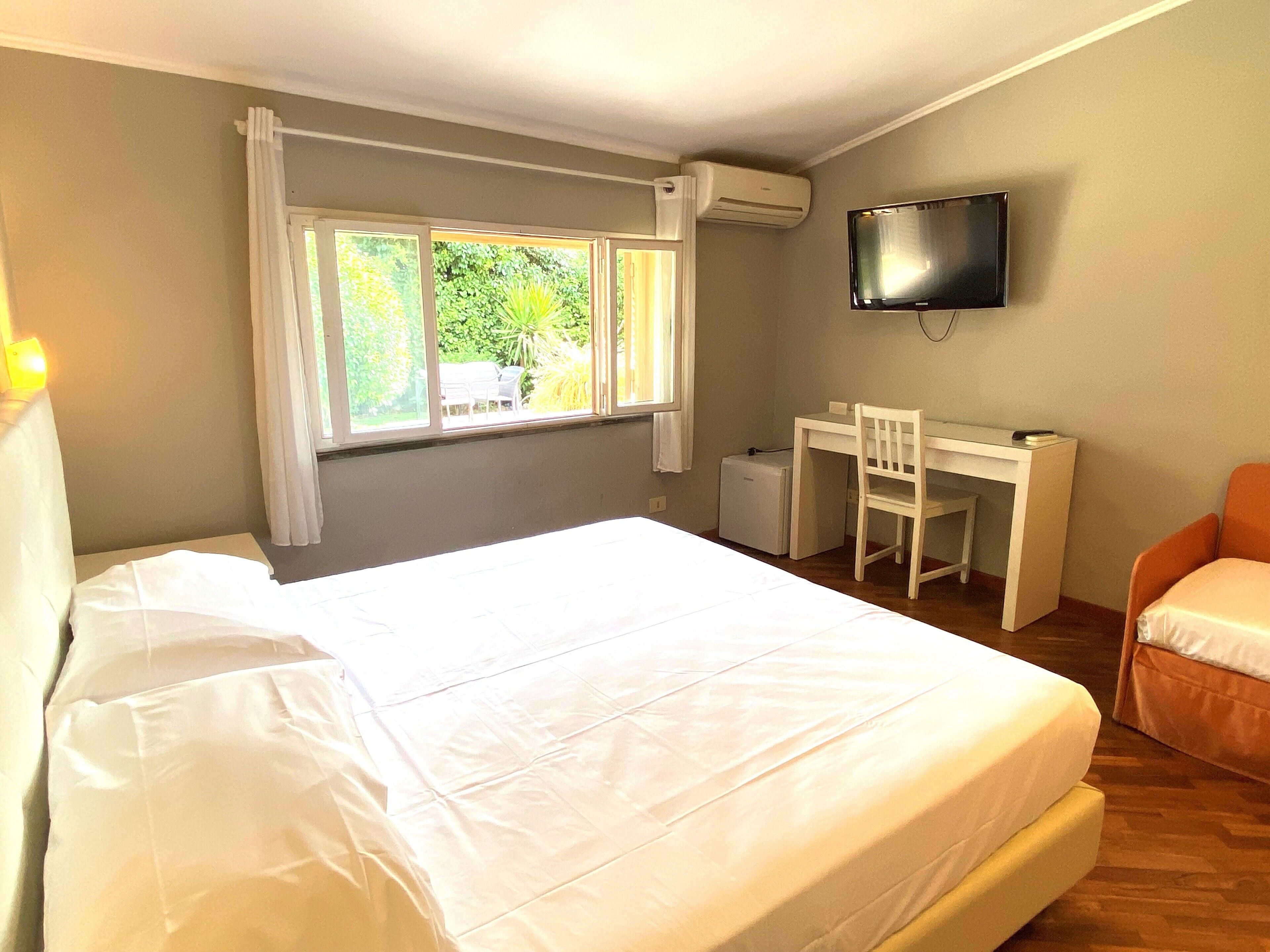Ein Schlafzimmer mit Bett, Schreibtisch, Stuhl, Fernseher und einem Fenster mit Vorhängen.