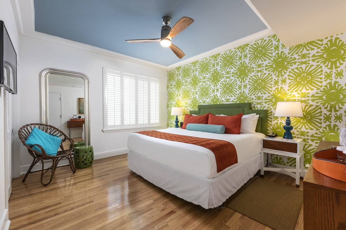 A bedroom with a bed, two nightstands, a ceiling fan, a chair, a mirror, and a window.