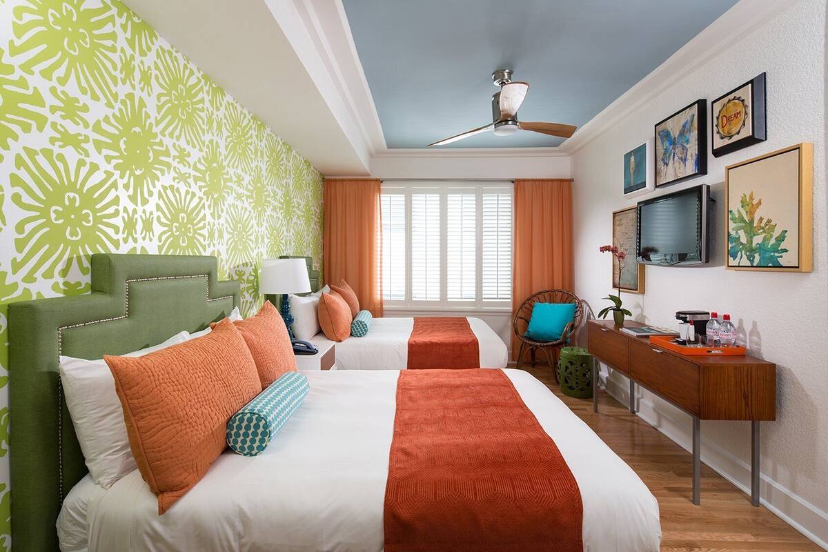 A hotel room with two beds, a desk, a chair, a television, and artwork on the wall.