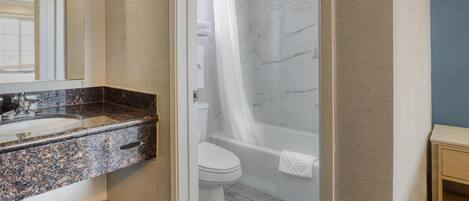 A bathroom with a granite countertop sink, a white toilet, and a bathtub with a shower curtain.