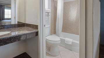 A bathroom with a granite countertop, a toilet, a bathtub, and a shower curtain.