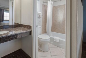 A bathroom with a granite countertop, a toilet, a bathtub, and a shower curtain.