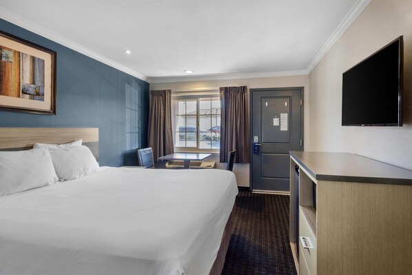 A hotel room with a large bed, a desk, a television, and a window with curtains.