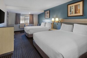 A hotel room with two beds, a desk, a TV, and a window with curtains.