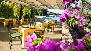 An outdoor dining area with yellow tables and chairs, a covered seating area, and a view of a pool and greenery. - Masseria San Domenico (Fasano)