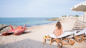 A beach with a row of sun loungers and a paddle boat. - Masseria San Domenico (Fasano)