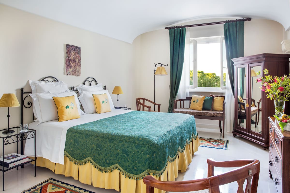 Un dormitorio con cama, mesitas de noche, una silla, cómoda y ventana con cortinas.