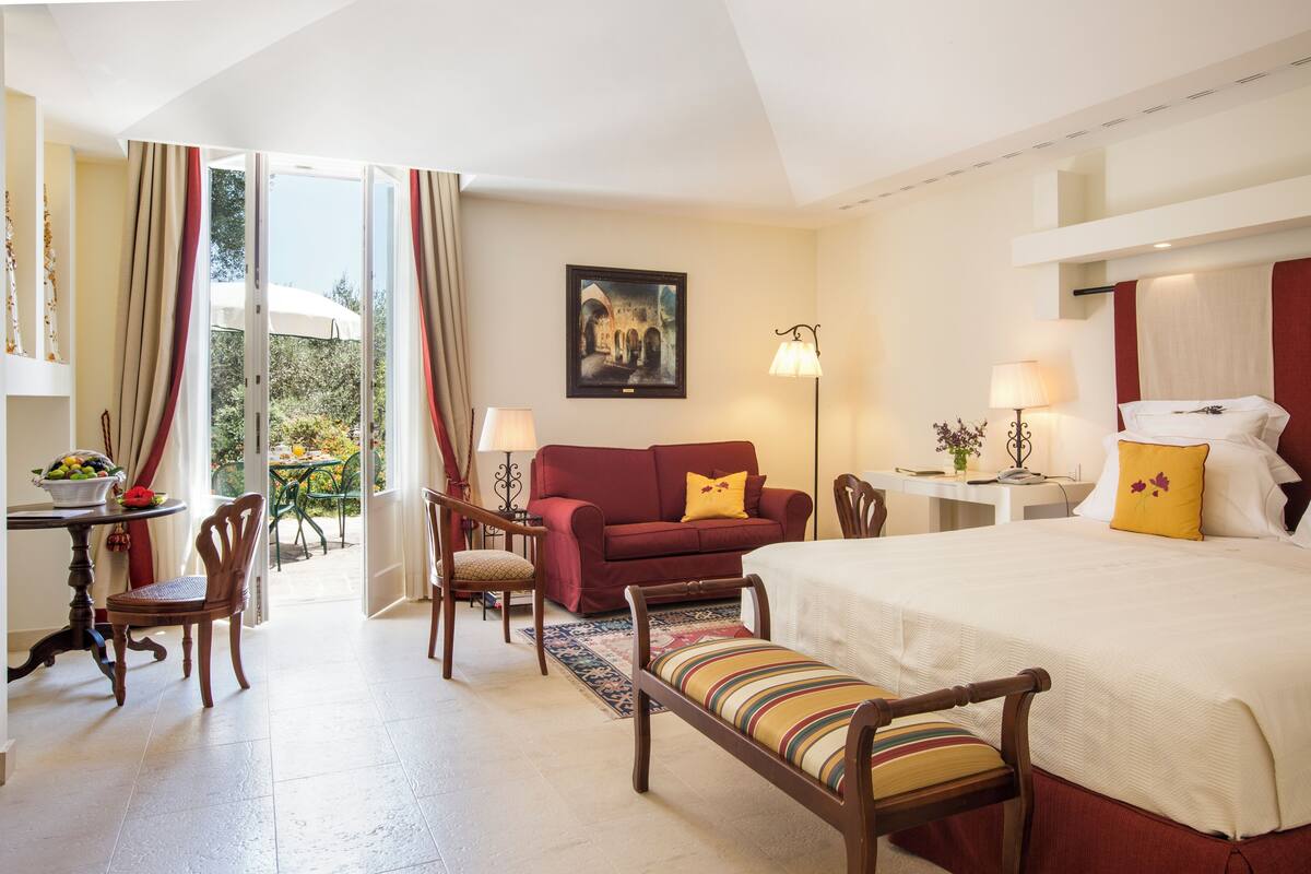 Habitación de hotel con cama, sofá, mesa de comedor con sillas, un escritorio pequeño y vistas al exterior.