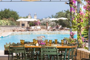 A poolside dining area with tables set for guests, surrounded by lush greenery and a clear blue pool. - Masseria San Domenico (Fasano)