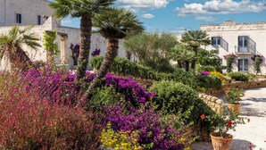 A courtyard with a stone wall, potted plants, and flowering shrubs. - Masseria San Domenico (Fasano)