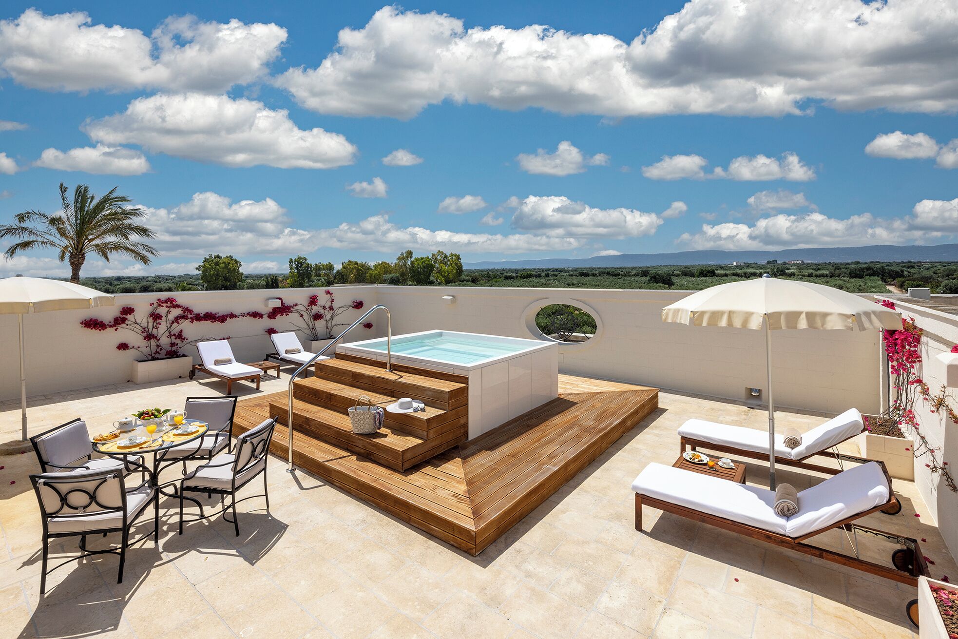 Une terrasse sur le toit équipée d’un jacuzzi, de chaises longues, d’une table à manger et offrant une vue sur le paysage.
