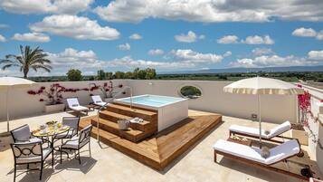 Une terrasse sur le toit équipée d’un jacuzzi, de chaises longues, d’une table à manger et offrant une vue sur le paysage.
