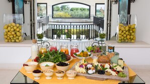 A breakfast buffet with a variety of fruits, cheeses, and breads, set against a balcony with a view of greenery. - Masseria San Domenico (Fasano)
