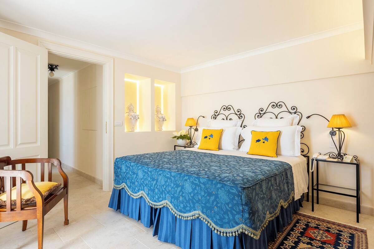 Un dormitorio con una cama, dos mesitas de noche, una silla y una puerta.