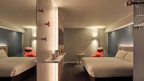 A hotel room with two beds, a small table, a chair, a mirror, and a wall-mounted shelf with a kettle and cups. - Holiday Inn Express London - Limehouse by IHG (London)