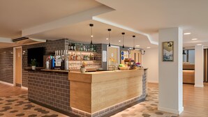 A bar area with a counter, shelves of bottles, and a seating area with a patterned floor. - Holiday Inn Express London - Limehouse by IHG (London)