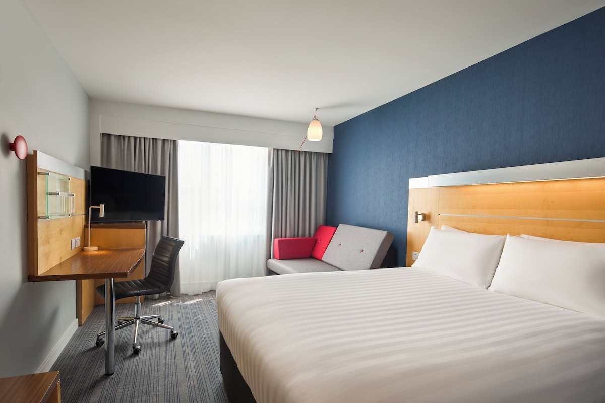 Una habitación de hotel con cama, escritorio con televisor, silla y sofá rojo.