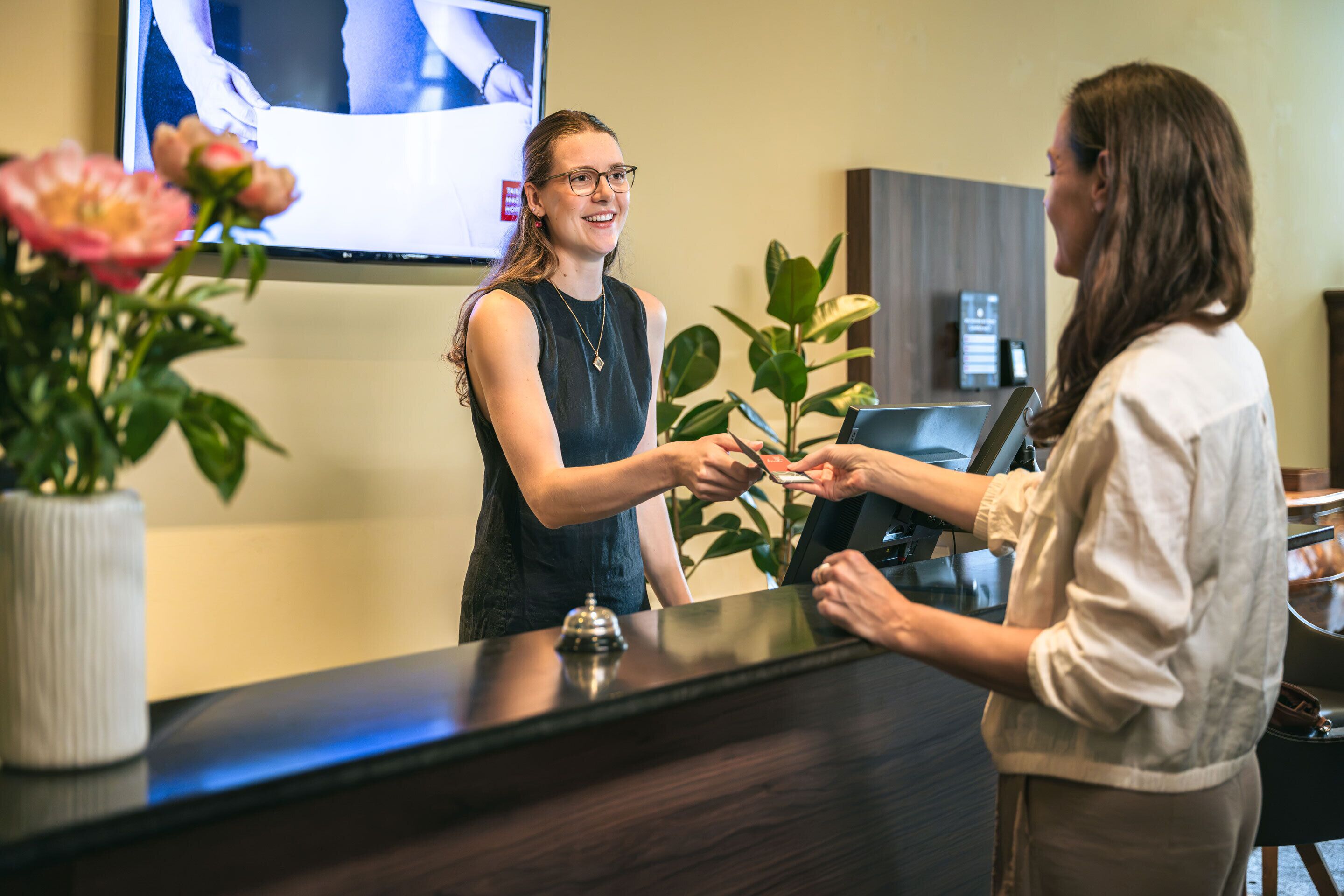 Una reception con uno schermo televisivo, una pianta e un vaso con fiori.
