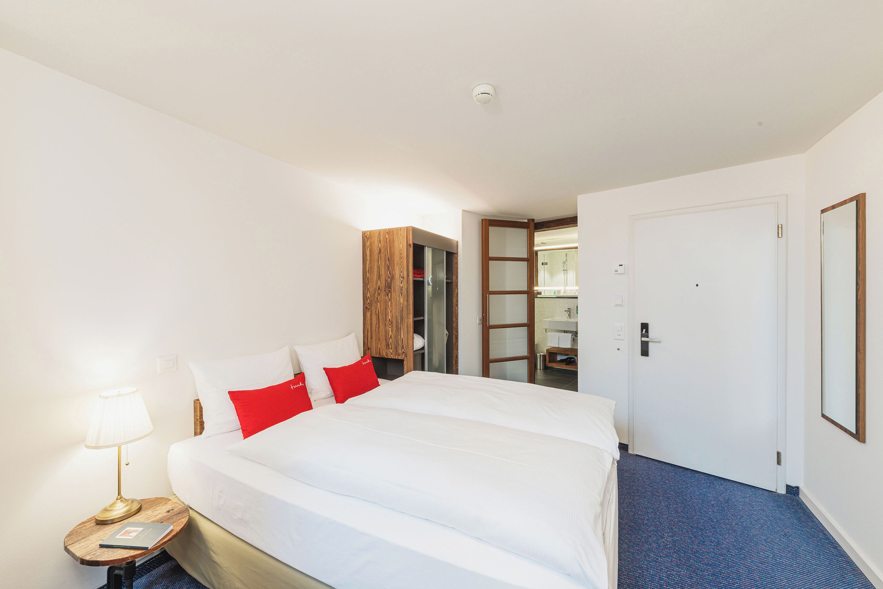 A hotel room with a large bed, a bedside table with a lamp, and a wardrobe.
