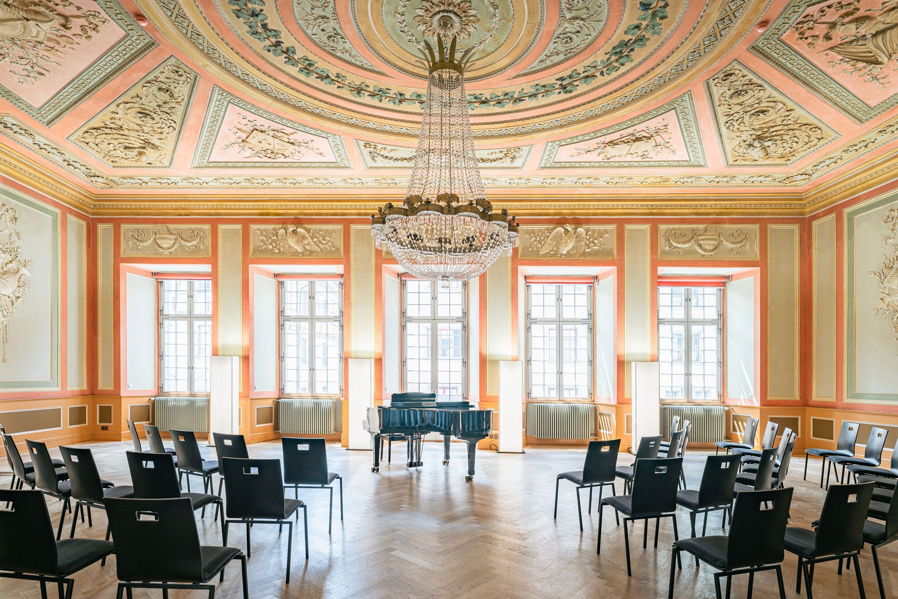 A grand hall with a large chandelier, ornate ceiling, and a piano.