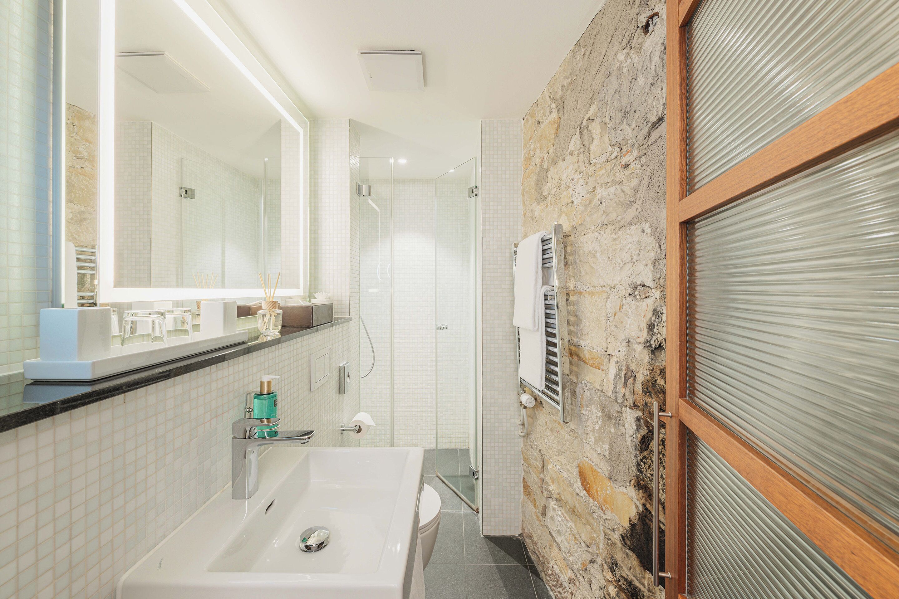 Un baño moderno con bañera, cabina de ducha de cristal y pared de piedra.