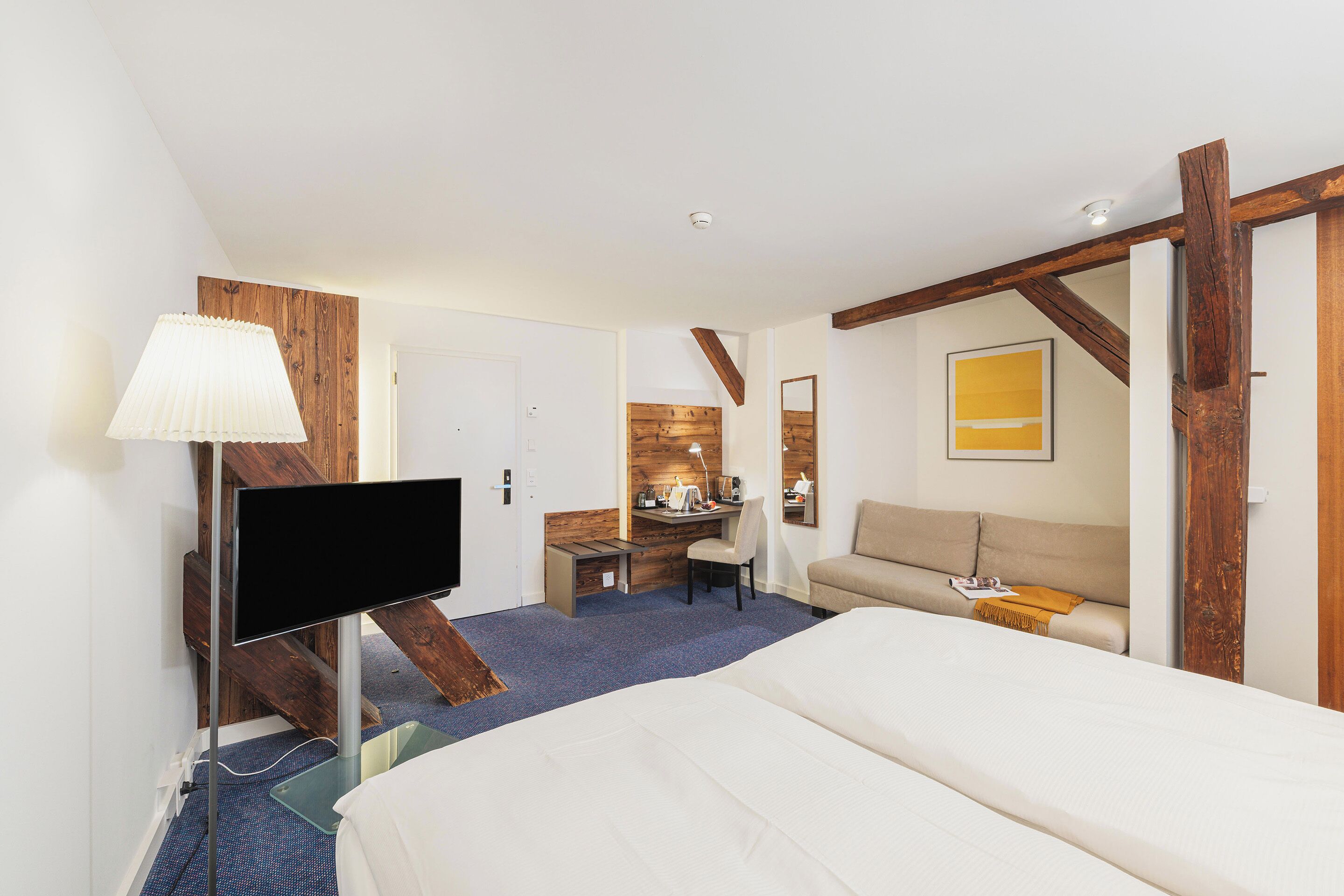 A hotel room with a bed, a desk, a chair, a TV, and a wooden accent wall.