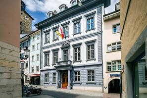 A historic building with a central entrance, multiple windows, and flags. - Tailormade Hotel RÜDEN Schaffhausen (Schaffhausen)