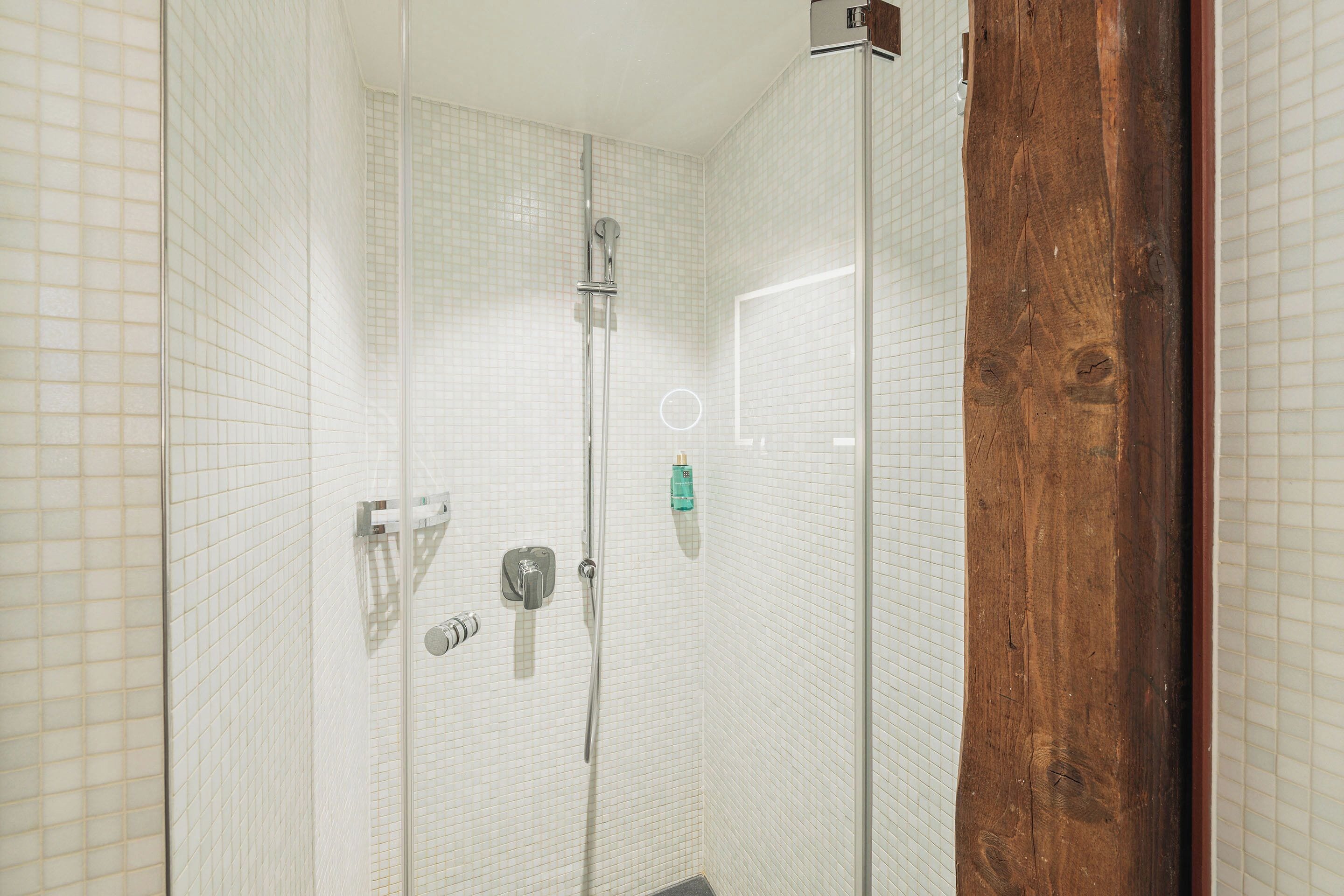 A glass-enclosed shower with tiled walls and a wooden door frame.