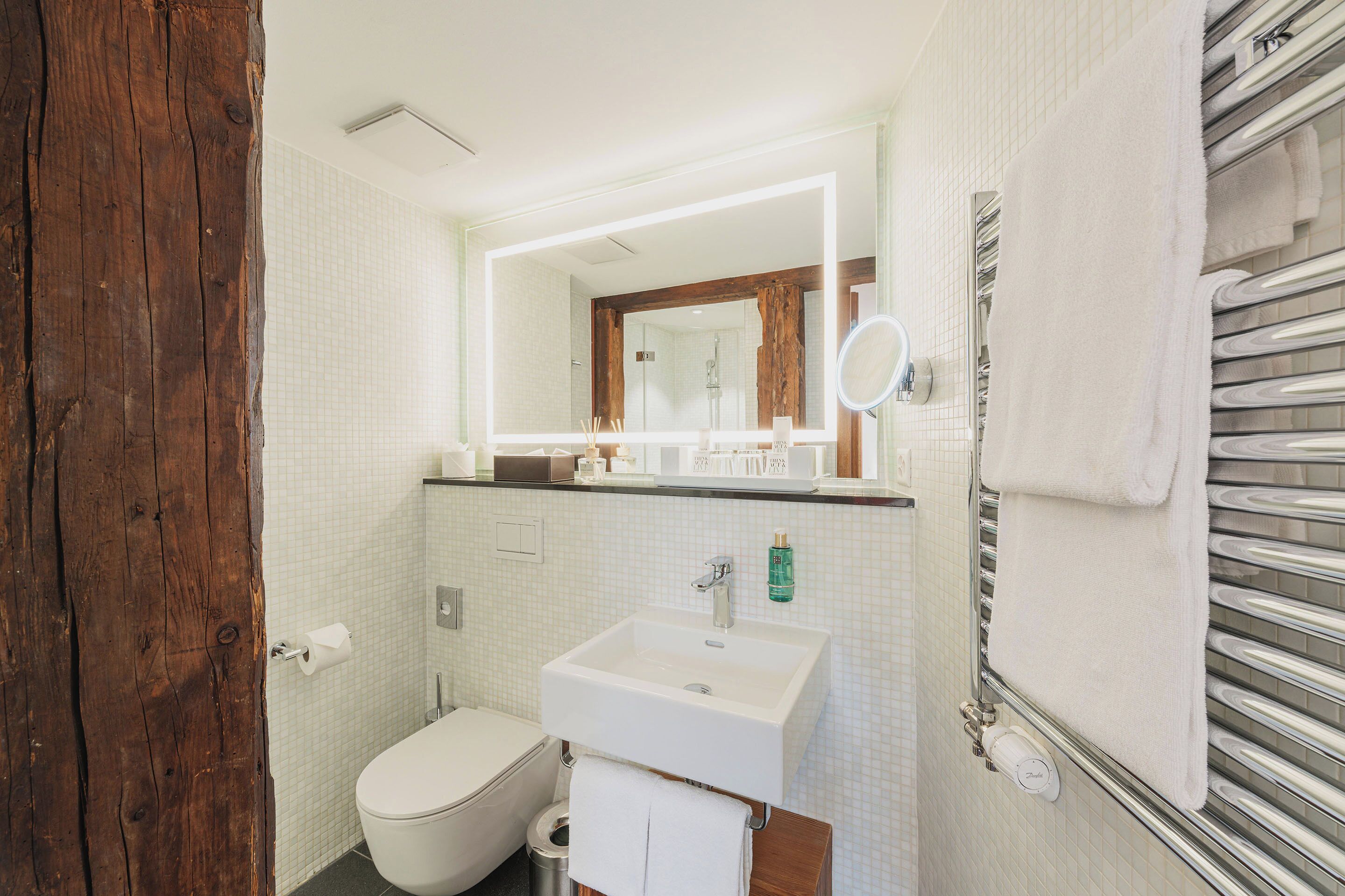 Une salle de bain avec une porte en bois, des carreaux blancs, un lavabo blanc, un miroir et un porte-serviettes.