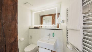 Une salle de bain avec une porte en bois, des carreaux blancs, un lavabo blanc, un miroir et un porte-serviettes.