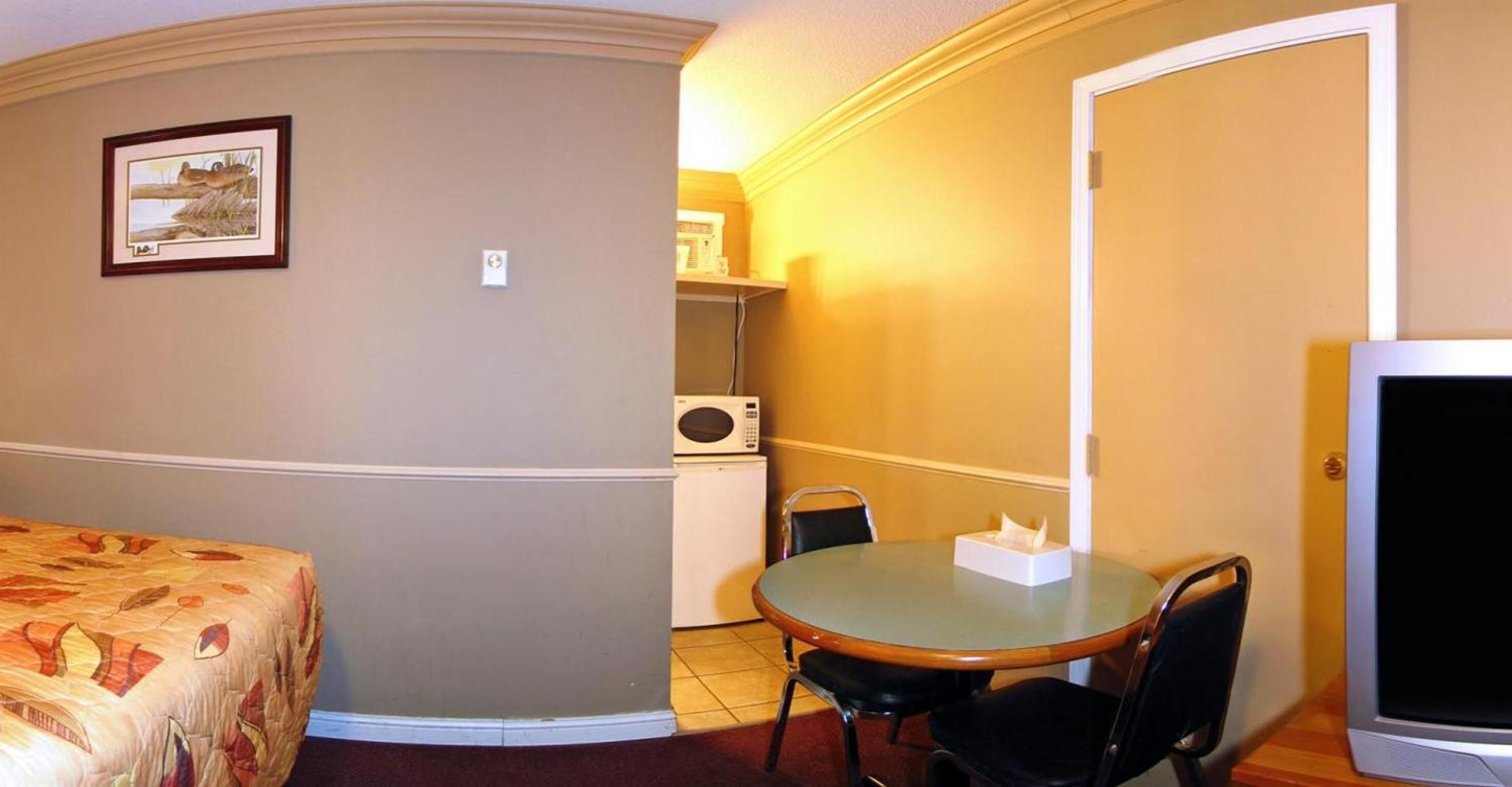Una habitación de hotel con una cama, una pequeña mesa con sillas, un microondas y un televisor.