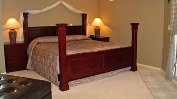 A four-poster bed with a canopy, two bedside lamps, a wooden nightstand, and a tufted leather ottoman.